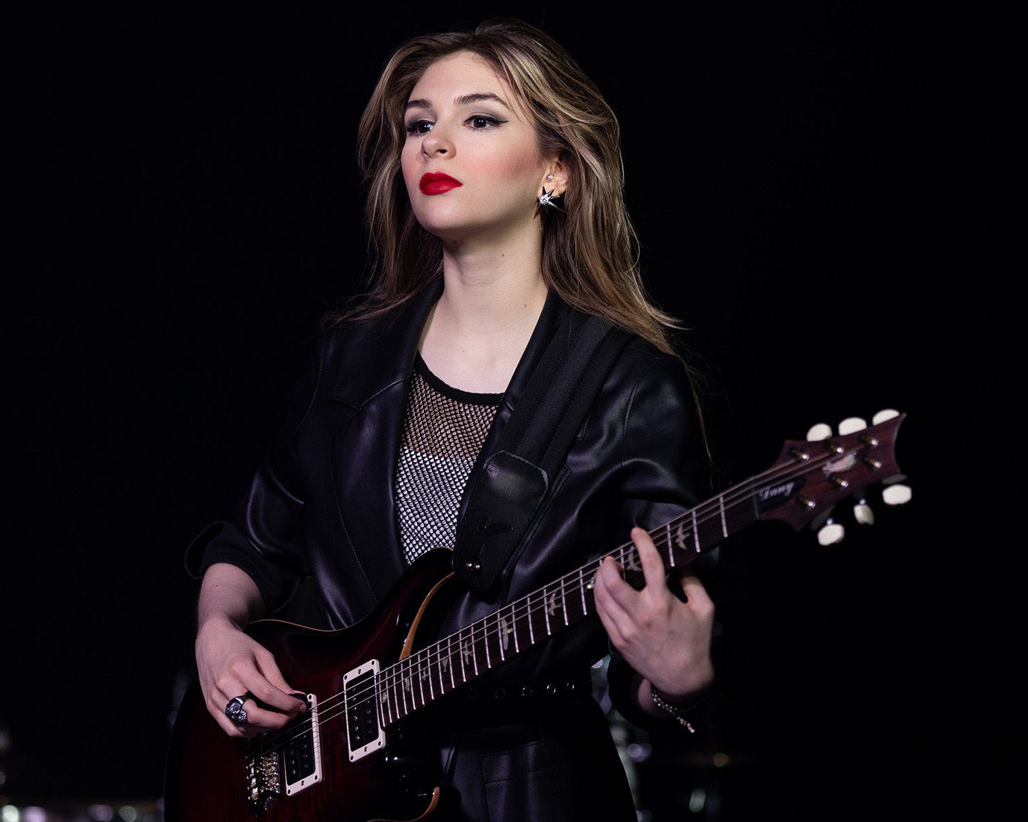 Woman playing a guitar against a black background